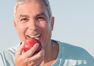 elderly man biting into a red apple 