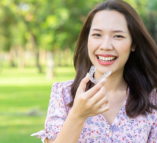 Smiling woman holding Invisalign in Raleigh