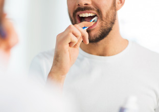 Man smiling while brushing his teeth in bathroom