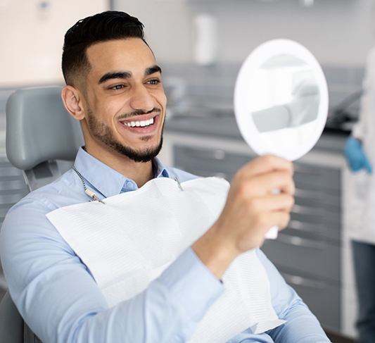 Dental patient looking in mirror, admiring the results of his cosmetic treatment