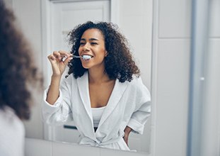 woman in a white bathrobe brushing her teeth 