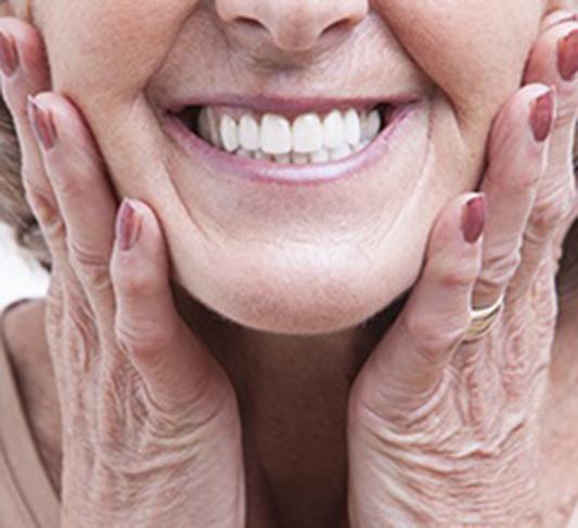 close-up of an elderly woman holding the sides of her face and smiling 
