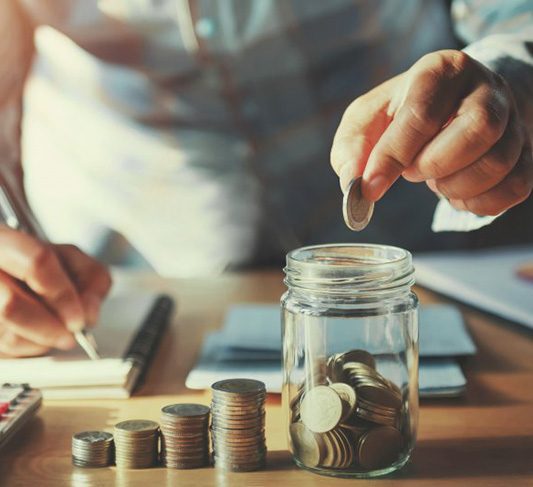 Man dropping a coin into a glass jar that’s sitting next to stacks of coins