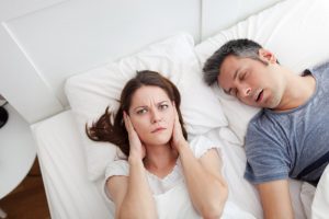 A woman covering her ears in bed due to her snoring partner.