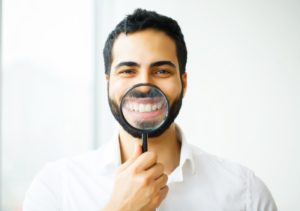 man holding magnifying glass to his teeth straightened by cosmetic dentist in Raleigh 