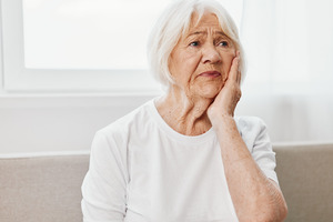 Woman in white shirt rubbing jaw in concern