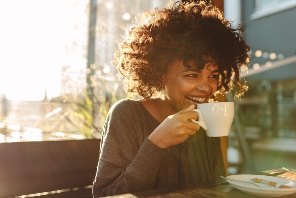 Woman smiling while enjoying a cup of coffee outside