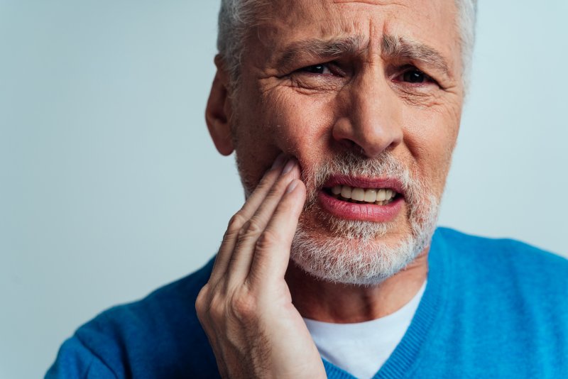 Elderly man putting his hand on his right cheek wincing at a toothache