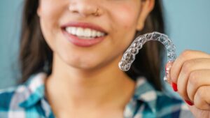 Smiling young woman holding Invisalign aligner 