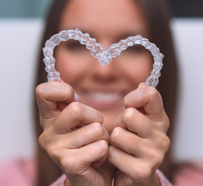 Woman holding clear aligners in a heart shape.
