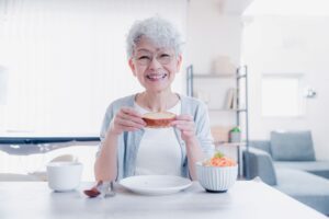 Woman with short curly gray hair at table eating slice of soft bread